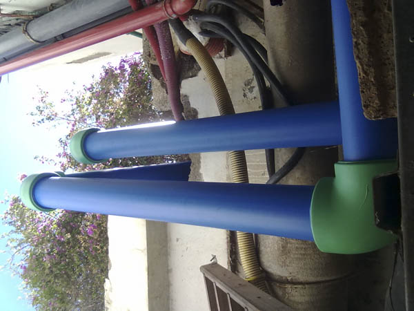 Instalaciones de fontanería, tubos azules y verdes, fondo con arbusto de flores rosas